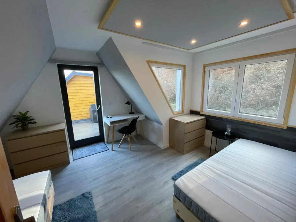 A Calm Resort világos, tetőtéri vendégszobája nagy ablakokkal, letisztult bútorokkal, íróasztallal és természetes fényben úszó, modern kialakítással